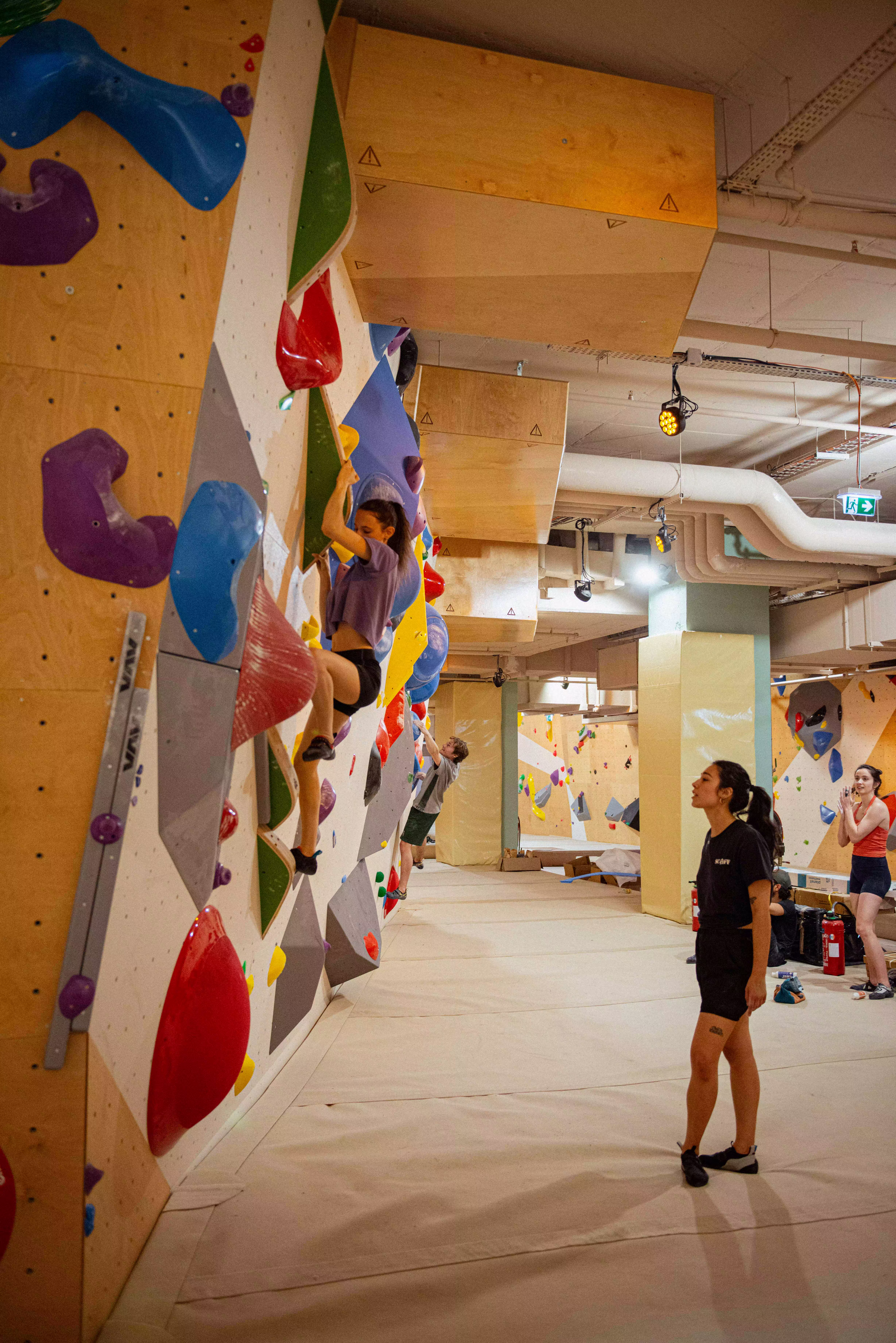 Coach et pratiquants observant une grimpeuse sur le mur.